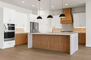 Kitchen featuring white cabinetry, sink, stainless steel fridge, and a center island with sink