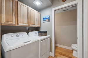 Clothes washing area with washing machine and dryer and light wood-type flooring