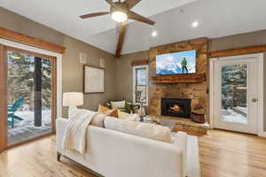 Living room featuring vaulted ceiling, ceiling fan, a fireplace, and light hardwood / wood-style floors