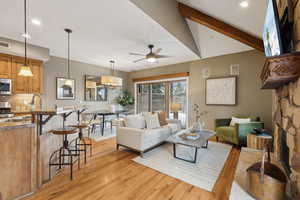 Living room featuring ceiling fan, vaulted ceiling with beams, a fireplace, and light wood-type flooring