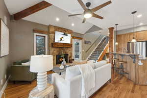 Living room with sink, light hardwood / wood-style flooring, ceiling fan, vaulted ceiling with beams, and a stone fireplace