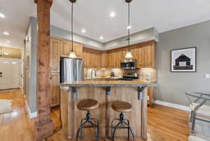 Kitchen with pendant lighting, light hardwood / wood-style flooring, appliances with stainless steel finishes, a kitchen breakfast bar, and tasteful backsplash