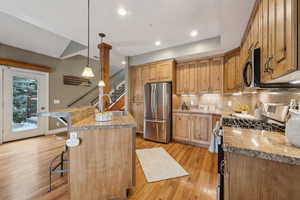 Kitchen featuring decorative light fixtures, appliances with stainless steel finishes, a kitchen breakfast bar, an island with sink, and backsplash