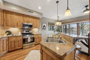 Kitchen featuring a breakfast bar, an island with sink, sink, hanging light fixtures, and stainless steel appliances