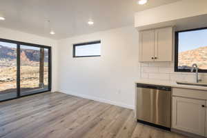 Kitchen featuring sink, white cabinetry, light wood-type flooring, dishwasher, and backsplash