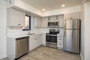 Kitchen featuring stainless steel appliances, light hardwood / wood-style floors, sink, and backsplash