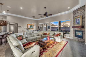 Living room featuring ornamental molding, a fireplace, and ceiling fan with notable chandelier