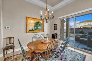 Dining area with an inviting chandelier, ornamental molding, and light tile patterned flooring