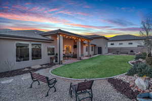 Back house at dusk featuring a lawn and a patio area