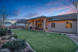 Back house at dusk featuring an outdoor living space, a patio, and a lawn