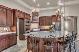 Kitchen with a kitchen island, decorative backsplash, hanging light fixtures, built in appliances, and light stone countertops