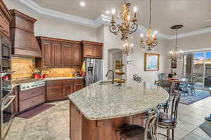 Kitchen featuring a kitchen bar, sink, a large island with sink, custom range hood, and stainless steel appliances