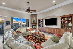 Tiled living room featuring ceiling fan, ornamental molding, and a stone fireplace