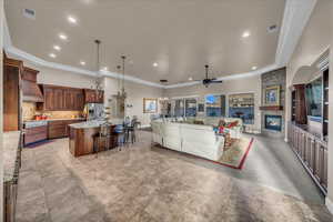 Living room with crown molding, a stone fireplace, and ceiling fan with notable chandelier