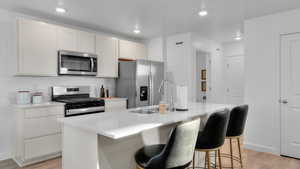 Kitchen featuring white cabinetry, sink, light hardwood / wood-style floors, stainless steel appliances, and a center island with sink