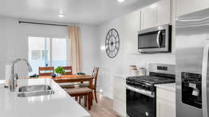 Kitchen with stainless steel appliances, white cabinetry, sink, and light wood-type flooring