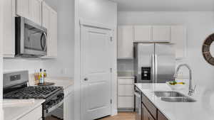 Kitchen featuring appliances with stainless steel finishes, white cabinetry, sink, light stone counters, and light hardwood / wood-style floors