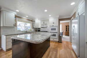 Kitchen with sink, white appliances, crown molding, white cabinetry, and a kitchen island