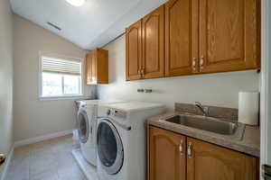 Vaulted laundry area with sink, washer and clothes dryer, cabinets, and light tile patterned flooring