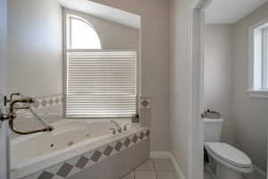 Primary bathroom featuring tile patterned floors, toilet, and tiled jetted tub