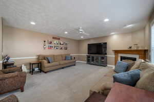 Living room featuring ceiling fan, a fireplace, light carpet, and a textured ceiling