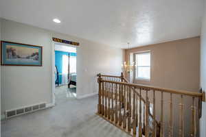 Hallway with an inviting chandelier, a textured ceiling, plenty of natural light, and light carpet