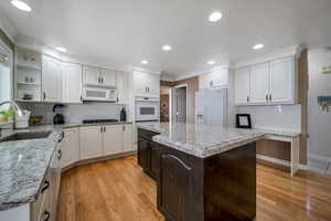 Kitchen with white cabinetry, sink, light hardwood / wood-style floors, crown molding, and white appliances