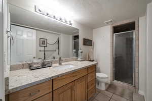 Bathroom with walk in shower, toilet, a textured ceiling, vanity, and tile patterned flooring