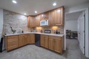 Kitchen with black dishwasher, sink, light stone counters, and decorative backsplash