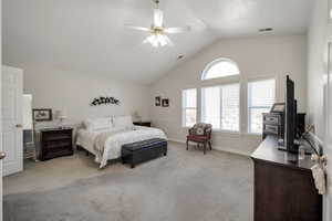 Primary bedroom with ceiling fan, light colored carpet, and lofted ceiling