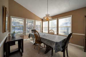 Carpeted dining room with lofted ceiling, a notable chandelier, and a textured ceiling