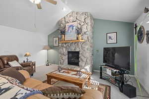 Living room with ceiling fan, a fireplace, vaulted ceiling, and carpet flooring