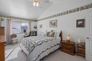 Carpeted bedroom featuring ceiling fan and vaulted ceiling