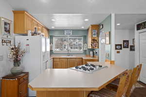 Kitchen featuring sink, white appliances, a breakfast bar area, a textured ceiling, and kitchen peninsula