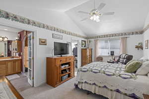 Bedroom with connected bathroom, lofted ceiling, sink, light colored carpet, and ceiling fan