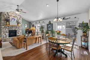 Dining space featuring ceiling fan with notable chandelier, lofted ceiling, hardwood / wood-style floors, and a fireplace