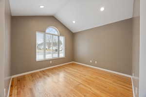 Empty room with vaulted ceiling and light hardwood / wood-style flooring