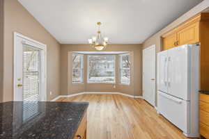 Kitchen featuring an inviting chandelier, light hardwood / wood-style flooring, dark stone countertops, white refrigerator, and pendant lighting