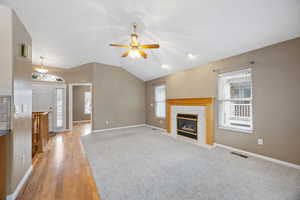 Unfurnished living room featuring a tiled fireplace, vaulted ceiling, ceiling fan, and plenty of natural light