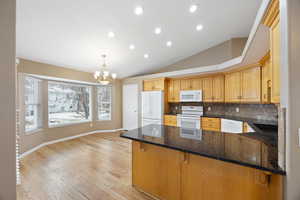 Kitchen featuring decorative light fixtures, dark stone countertops, white appliances, and kitchen peninsula