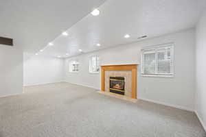 Unfurnished living room with a tiled fireplace, light colored carpet, and a textured ceiling