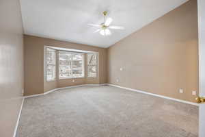 Empty room featuring vaulted ceiling, carpet, and ceiling fan