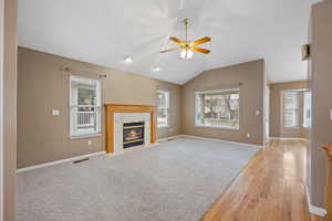 Unfurnished living room with ceiling fan, lofted ceiling, a fireplace, and light carpet