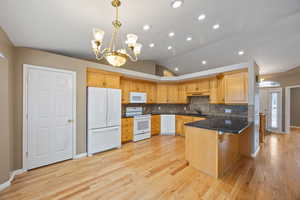 Kitchen featuring pendant lighting, lofted ceiling, white appliances, backsplash, and light wood-type flooring