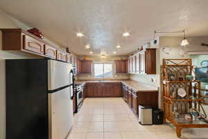 Kitchen featuring stainless steel appliances, sink, light tile patterned floors, and a textured ceiling