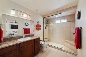 Bathroom featuring a tile shower, tile patterned flooring, vanity, toilet, and a textured ceiling