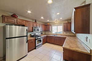 Kitchen with sink, light tile patterned floors, stainless steel appliances, and a textured ceiling