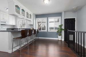 Kitchen with dark wood-type flooring, a breakfast bar, sink, white appliances, and white cabinets