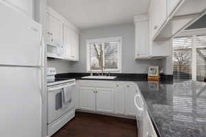 Kitchen featuring white appliances, dark stone counters, sink, and white cabinets