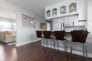 Kitchen with a kitchen breakfast bar, dark hardwood / wood-style flooring, white cabinets, and white appliances